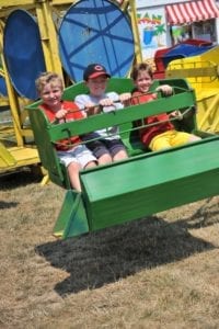 Three young boys sit in car of green carnival ride