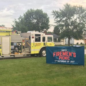 Yellow fire truck and Firemen's Picnic sign in grass